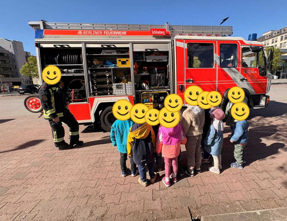 Die Kinder stehen vor einem Feuerwehrauto der Berliner Feuerwehr und lassen sich die Ausrüstung zeigen