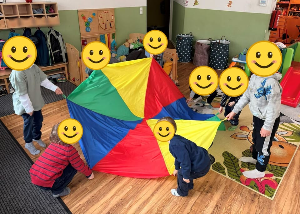 Kinder spielen gemeinsam mit einem bunten Schwungtuch im Gruppenraum