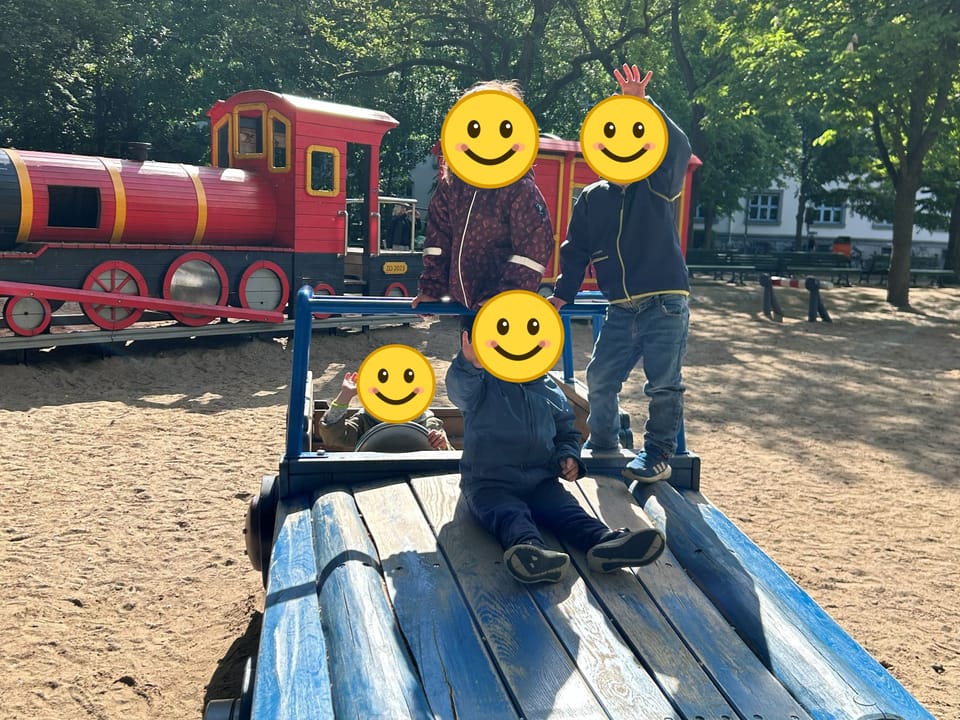 Vier Kinder spielen auf einem Holzauto, dahinter steht eine Spielplatz-Lokomotive